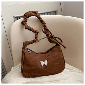 Detail of a brown pleated shoulder bag with silver butterfly emblem on silk fabric