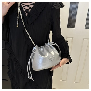 Detailed view of silver metallic drawstring bucket bag with triangular metal logo plaque