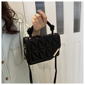 Detail of black quilted handbag featuring a unique knotted handle and gold metal corner trim