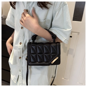 Detail of black quilted crossbody bag with gold buckle and knotted top handle worn by model