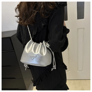 Detail view of silver drawstring bucket bag featuring metal chain strap and logo plaque