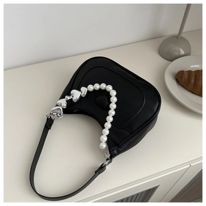 Detail of black heart-shaped handbag featuring faux pearl strap and silver heart pendants