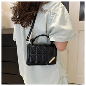 Detail of black quilted geometric textured handbag with gold metal bar and top handle