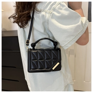 Detail of black geometric quilted handbag with knotted handle and gold metal trim