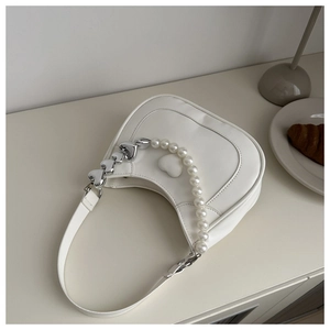 Close-up of white hobo bag with pearl chain and embossed heart detail in a lifestyle setting