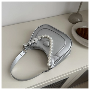 Detail of silver heart-embossed half-moon bag with large pearl and heart charms handle