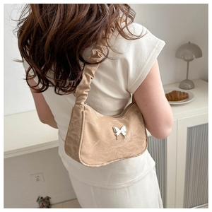 Chic beige underarm bag with silver butterfly charm shown in a cozy lifestyle setting