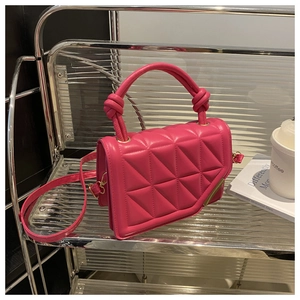 Detail of rose red quilted handbag with knot handle and detachable strap on shelf