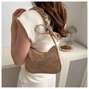Detail of a ruffled beige shoulder bag with silver butterfly charm and bow strap accents