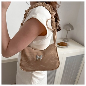 Detail of khaki pleated underarm bag with silver metal butterfly and ruffled strap on shoulder