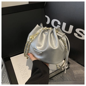 Close-up of silver bucket bag featuring metallic texture, gold chain and drawstring closure