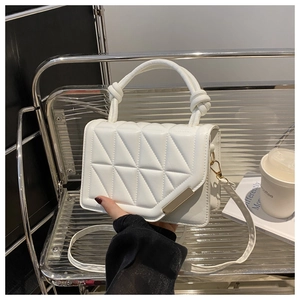Close-up of a white quilted handbag with a gold metal trim on a modern metal chair