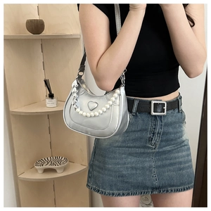 Detail of silver heart embossed shoulder bag with pearl chain and metallic heart charm