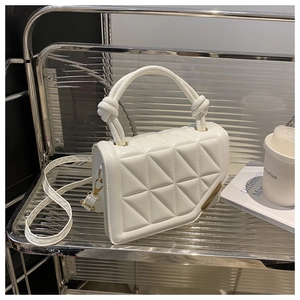 Detail of white quilted crossbody bag with knot handle and gold hardware on glass shelf