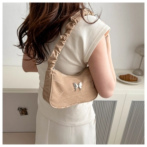 Close-up of beige shoulder bag with silver butterfly accent and scrunchie strap detail