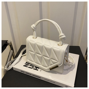 Detail of white quilted crossbody bag with knotted handle and gold clasp on a book