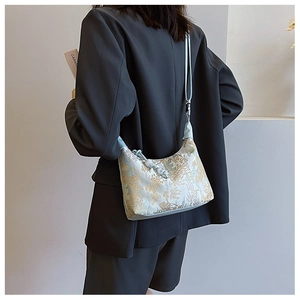 Detail of light blue silk jacquard crossbody bag with golden floral patterns on a model