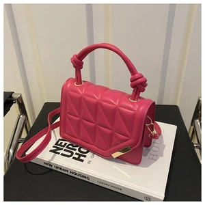 Detail of rose red quilted crossbody bag with knotted handle on a white book