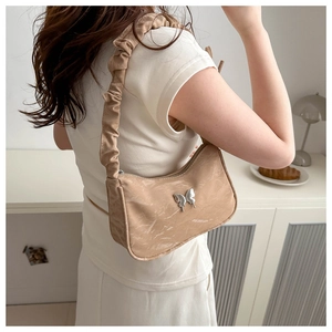Detail of a chic shoulder bag featuring a silver butterfly charm and pleated strap design