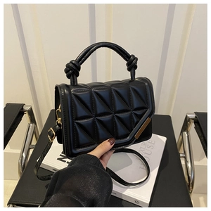 Close-up of black quilted leather handbag with knot handle and gold hardware on white pedestal