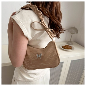 Detail of beige scrunchie shoulder bag featuring a silver metal butterfly and pleated texture