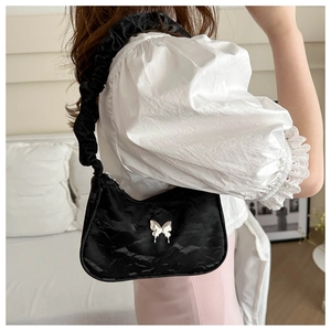 Detail of black satin underarm bag with silver butterfly buckle and scrunchie shoulder strap