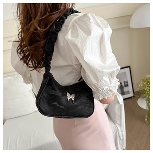 Detail of black velvet pleated shoulder bag with silver butterfly charm on a model