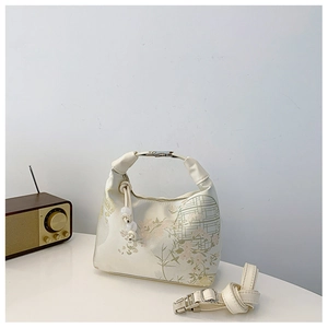 Detail of cream handbag with floral patterns, silver buckle, and pearl bead charm