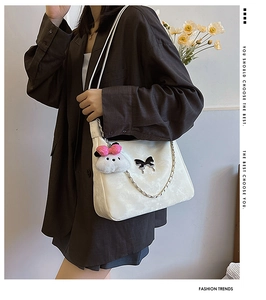 White shoulder bag with black bow badge, silver chain, and cute plush charm detail