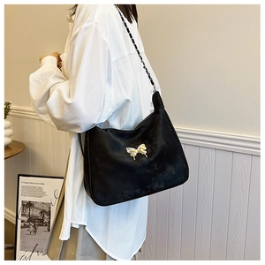 Detail of black hobo bag with golden butterfly buckle and chain strap shown on shoulder