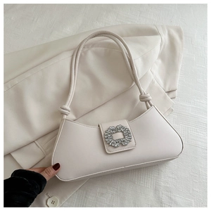 Close-up of cream shoulder bag featuring a sparkling crystal-encrusted circular buckle detail