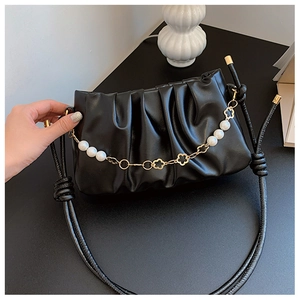 Detail of black ruched cloud bag with pearl and floral chain strap on dark tabletop