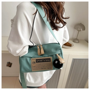 Detail of teal canvas cylindrical crossbody sports bag with fuzzy coal sprite charm