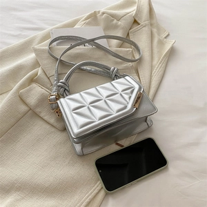 Silver quilted crossbody bag with knot handle and adjustable strap on beige blazer