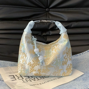 Modern light blue silk handbag with floral patterns and pearl charm displayed on newspaper