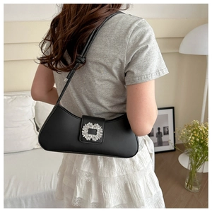 Detail view of a black leather baguette bag with a sparkling crystal square buckle on shoulder