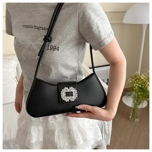 Detail of elegant black shoulder bag featuring a crystal flower buckle in a home setting