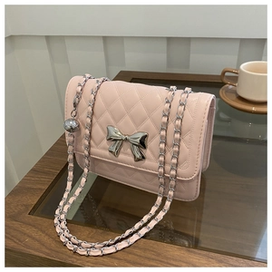 Detail of pink quilted shoulder bag with silver metal bow and chain strap on a table
