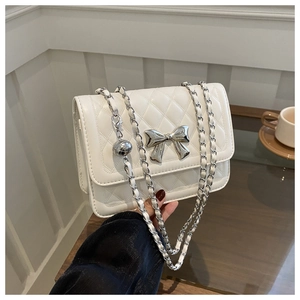 Close-up of quilted white crossbody bag with silver bow accent and chain strap