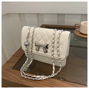Detail shot of a beige quilted chain bag featuring a metallic silver bow on the side