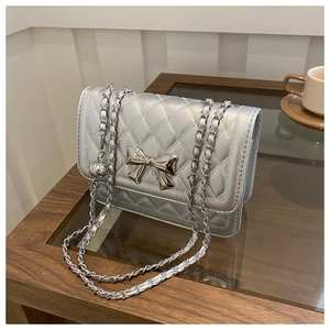 Detail of silver quilted shoulder bag featuring a metallic bow and chain strap in a cafe setting