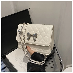 Detail shot of white quilted leather bag with silver bow buckle and chain strap