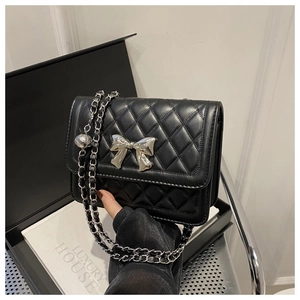 Macro shot of a quilted black leather bag with a silver bow clasp and chain strap