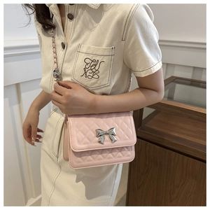 Pink quilted shoulder bag with silver bow detail worn by a model in a cozy interior