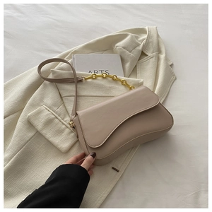 Detail of minimalist beige moon bag with chunky gold chain strap and smooth leather texture
