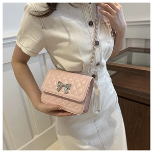 Detail of pink quilted shoulder bag featuring silver bow clasp and chain strap on model