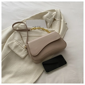 Detail of a beige leather flap bag featuring a gold chunky chain on a cream blazer