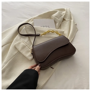 Detail of dark brown leather crescent bag with golden chain strap on white blazer