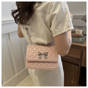 Detail of pink quilted shoulder bag with silver bow buckle and chain strap shown on model