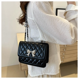 Close-up of black quilted shoulder bag featuring a silver bow and metal chain strap